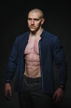 Tarz sahibi, kel genç bir adam çıplak bir gövdeyle kategoride karanlık bir arkaplanda duruyor.