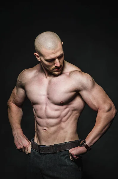 Sportif seksi adam karanlık bir zeminde üstsüz duruyor. Spor, güzellik