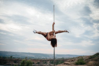 Genç ve seksi bir kız güzel bir günbatımında direğin üzerinde inanılmaz egzersizler yapıyor. Dans edelim. Cinsellik