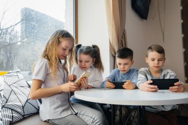 Çocuklar bir kafede bir masada oturup birlikte cep telefonu oynarlar. Modern eğlence