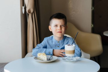 Küçük tatlı bir çocuk bir kafede oturuyor ve bir kek ve kakaoya yakından bakıyor. Diyet ve uygun beslenme