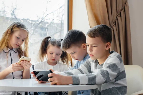子供たちはカフェのテーブルに座り 携帯電話を一緒に再生します 近代芸能 — ストック写真