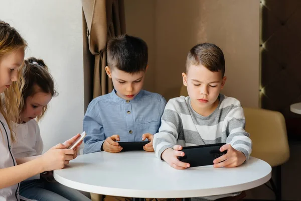 孩子们坐在咖啡馆的桌子旁 一起玩手机 现代娱乐 — 图库照片
