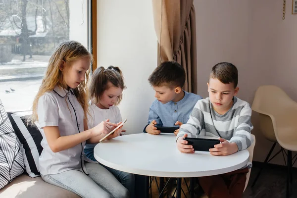 子供たちはカフェのテーブルに座り 携帯電話を一緒に再生します 近代芸能 — ストック写真