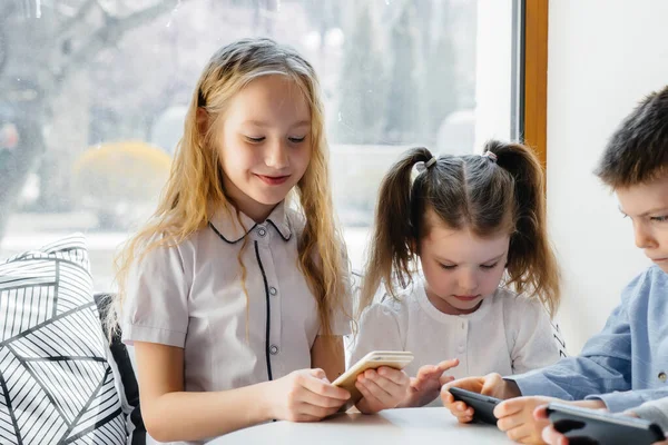 子供たちはカフェのテーブルに座り 携帯電話を一緒に再生します 近代芸能 — ストック写真