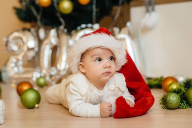 Sevimli gülümseyen bebek, Noel ağacının altında yatıyor ve hediyelerle oynuyor. Noel ve Yeni Yıl kutlamaları