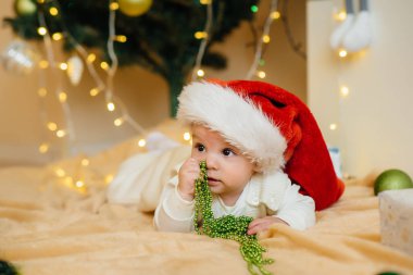 Sevimli gülümseyen bebek, Noel ağacının altında yatıyor ve hediyelerle oynuyor. Noel ve Yeni Yıl kutlamaları