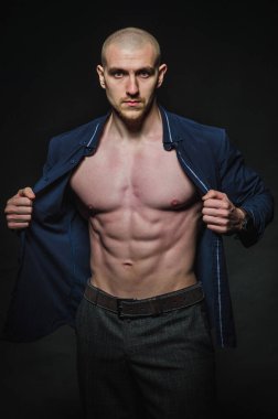 Tarz sahibi, kel genç bir adam çıplak bir gövdeyle kategoride karanlık bir arkaplanda duruyor.