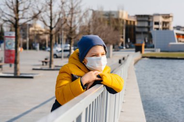 Bir çocuk, karantina sırasında maske takmış gri bir arka planda duruyor. Maskeli karantina
