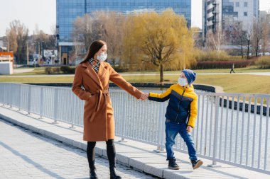 Genç bir aile, karantina ve salgın sırasında güneşli bir günde yürüyüp temiz hava soluyor. İnsanların yüzlerindeki maskeler.