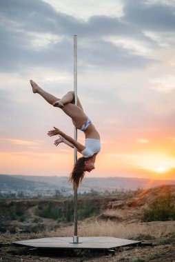 Genç ve seksi bir kız güzel bir günbatımında direğin üzerinde inanılmaz egzersizler yapıyor. Dans edelim. Cinsellik
