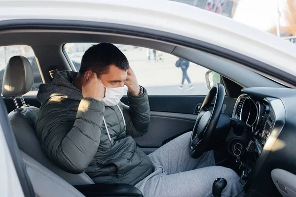 パンデミックとコロナウイルスの間 運転している間 若い男は個人的な安全のためにマスクをつけて車輪の後ろに座っています — ストック写真