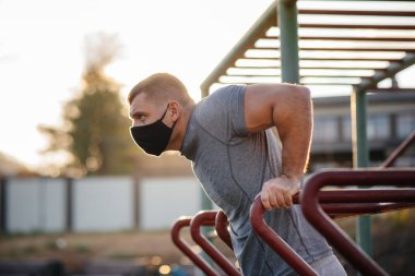 Genç bir adam gün batımında salgın sırasında spor sahasında maske takıp uyuşturucu kullanıyor. Spor, sağlıklı yaşam tarzı.