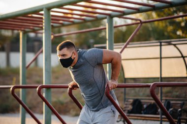 Genç bir adam gün batımında salgın sırasında spor sahasında maske takıp uyuşturucu kullanıyor. Spor, sağlıklı yaşam tarzı.