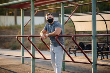 Genç bir adam gün batımında salgın sırasında spor sahasında maske takıp uyuşturucu kullanıyor. Spor, sağlıklı yaşam tarzı.