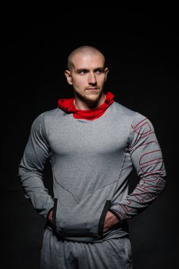 Stüdyoda kapüşonlu karanlık bir arka plana karşı duran sportif bir adam. Spor, güzellik