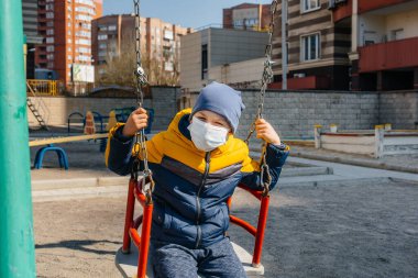 Karantina sırasında maskeli küçük bir çocuk oyun alanında yürüyor. Evde kal.