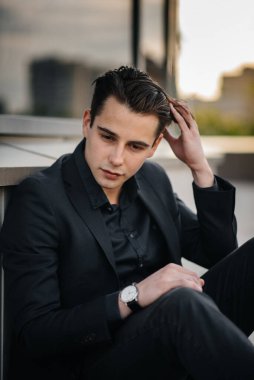 Şık bir genç adam gün batımında aynalı bir binanın yanında duruyor. Moda.