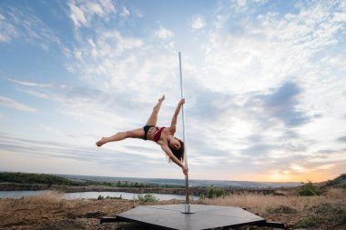 Genç ve seksi bir kız güzel bir günbatımında direğin üzerinde inanılmaz egzersizler yapıyor. Dans edelim. Cinsellik