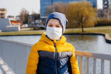 Bir çocuk, karantina sırasında maske takmış gri bir arka planda duruyor. Maskeli karantina