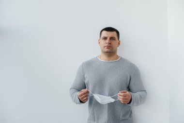 Genç bir adam, karantina sırasında maske takarak gri arka planda duruyor. Maskeli karantina