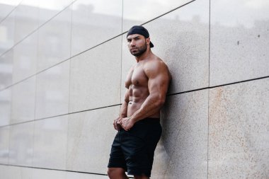 Seksi sporcu duvarın yanında üstsüz duruyor. Fitness, vücut geliştirme