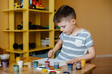 Odasında küçük sevimli bir çocuk oynuyor ve resim yapıyor. Eğlence ve eğlence. Evde kal.