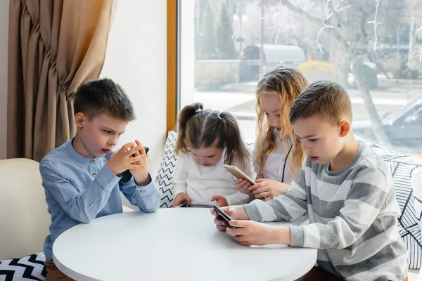 子供たちはカフェのテーブルに座り 携帯電話を一緒に再生します 近代芸能 — ストック写真