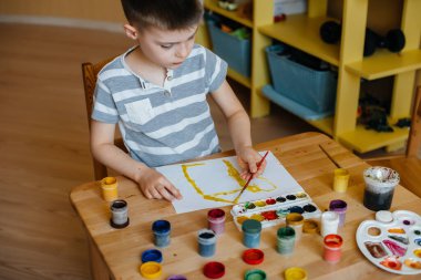 Odasında küçük sevimli bir çocuk oynuyor ve resim yapıyor. Eğlence ve eğlence. Evde kal.