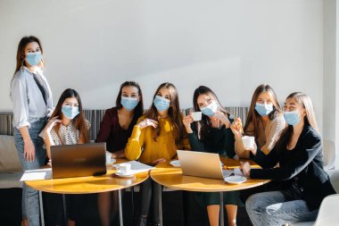 Maskeli bir grup kız bir kafede oturup dizüstü bilgisayarlarla çalışıyor. Öğrenciler.
