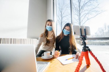 Maskeli bir kafede oturan iki genç kız video blogu yönetiyor. Kameraya iletişim..