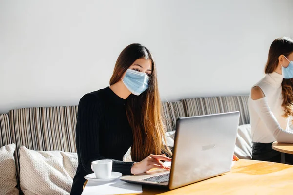 stock image A group of masked girls keep a social distance in a cafe when working on laptops.