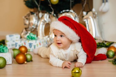 Sevimli gülümseyen bebek, Noel ağacının altında yatıyor ve hediyelerle oynuyor. Noel ve Yeni Yıl kutlamaları