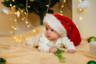 Sevimli gülümseyen bebek, Noel ağacının altında yatıyor ve hediyelerle oynuyor. Noel ve Yeni Yıl kutlamaları