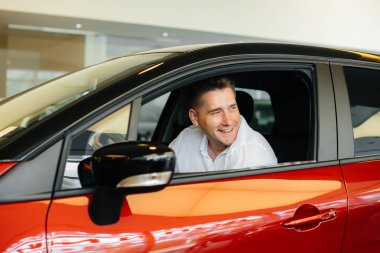 Genç bir adam yeni bir arabanın kabininde oturuyor ve onu test ediyor. Araba almak.