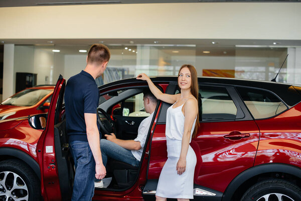 A happy young couple chooses and buys a new car at a car dealership. Buying a new car