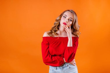 Genç ve güzel bir kız duygularını gösterir ve stüdyoda turuncu bir arka planda gülümser. Reklam için kızlar