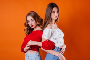 İki genç ve güzel kız, turuncu bir arka planda stüdyoda duygu ve gülümseme gösteriyor. Reklam için kızlar