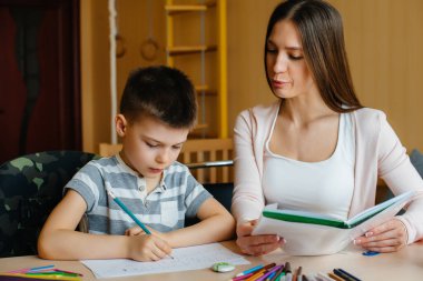 Genç bir anne evde oğluyla ev ödevi yapıyor. Ebeveynler ve eğitim
