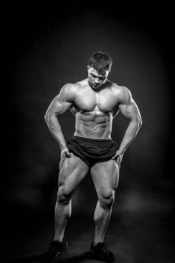 Stüdyoda siyah arka planda poz veren seksi genç bir atlet. Fitness, vücut geliştirme, siyah beyaz