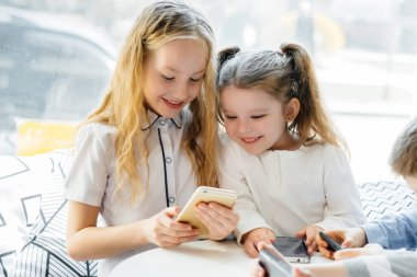 Çocuklar bir kafede bir masada oturup birlikte cep telefonu oynarlar. Modern eğlence