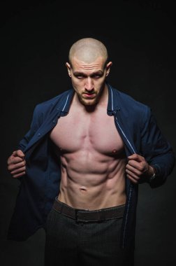 Tarz sahibi, kel genç bir adam çıplak bir gövdeyle kategoride karanlık bir arkaplanda duruyor.