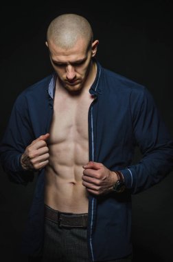 Tarz sahibi, kel genç bir adam çıplak bir gövdeyle kategoride karanlık bir arkaplanda duruyor.