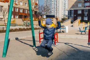Karantina sırasında maskeli küçük bir çocuk oyun alanında yürüyor. Evde kal.
