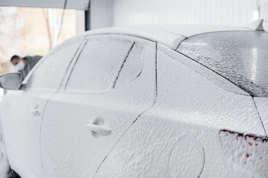 Köpüklü modern yıkama ve beyaz bir arabanın yüksek basınçlı suyu. Araba yıkama