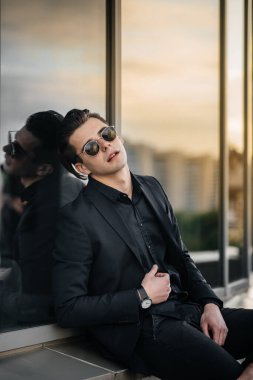 Şık bir genç adam gün batımında aynalı bir binanın yanında duruyor. Moda.