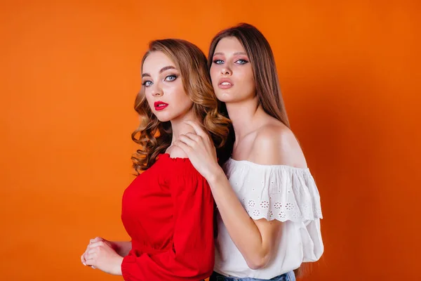 两个年轻貌美的女孩带着橙色的背景在演播室里表现出感情和微笑 女孩做广告 — 图库照片