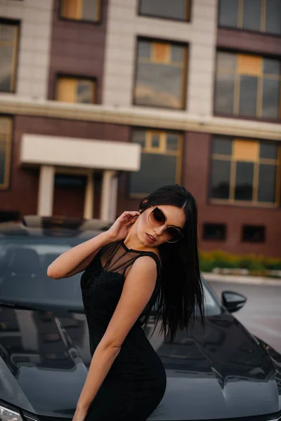 スタイリッシュな若い女の子は黒いドレスで車の近くに立っています ファッション スタイル — ストック写真