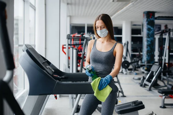 The girl in the mask disinfecting the gym equipment during a pandemic.