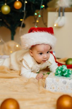 Sevimli gülümseyen bebek, Noel ağacının altında yatıyor ve hediyelerle oynuyor. Noel ve Yeni Yıl kutlamaları
